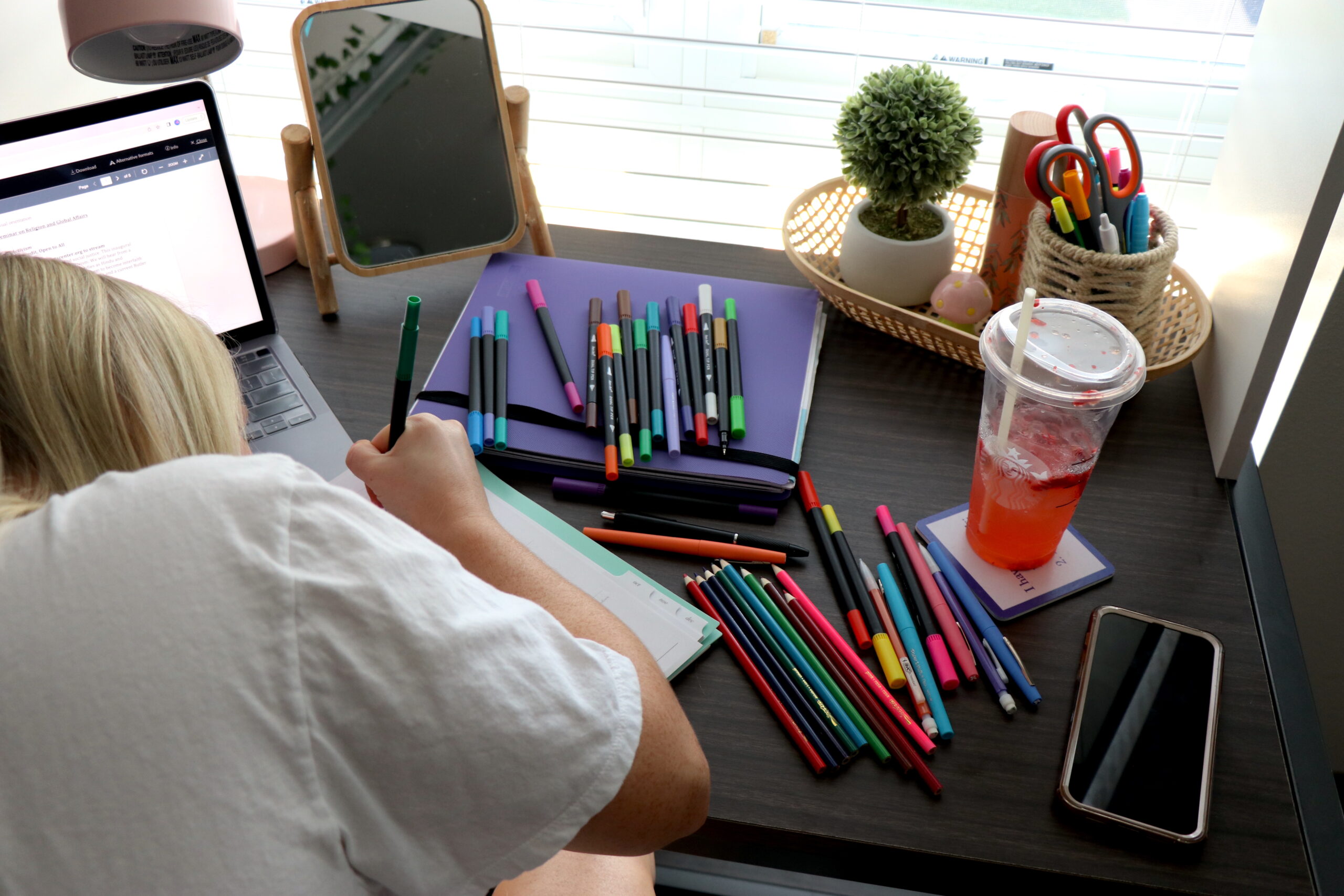 An artist's desk is in view as she works, with color pencils scattered amongst it.